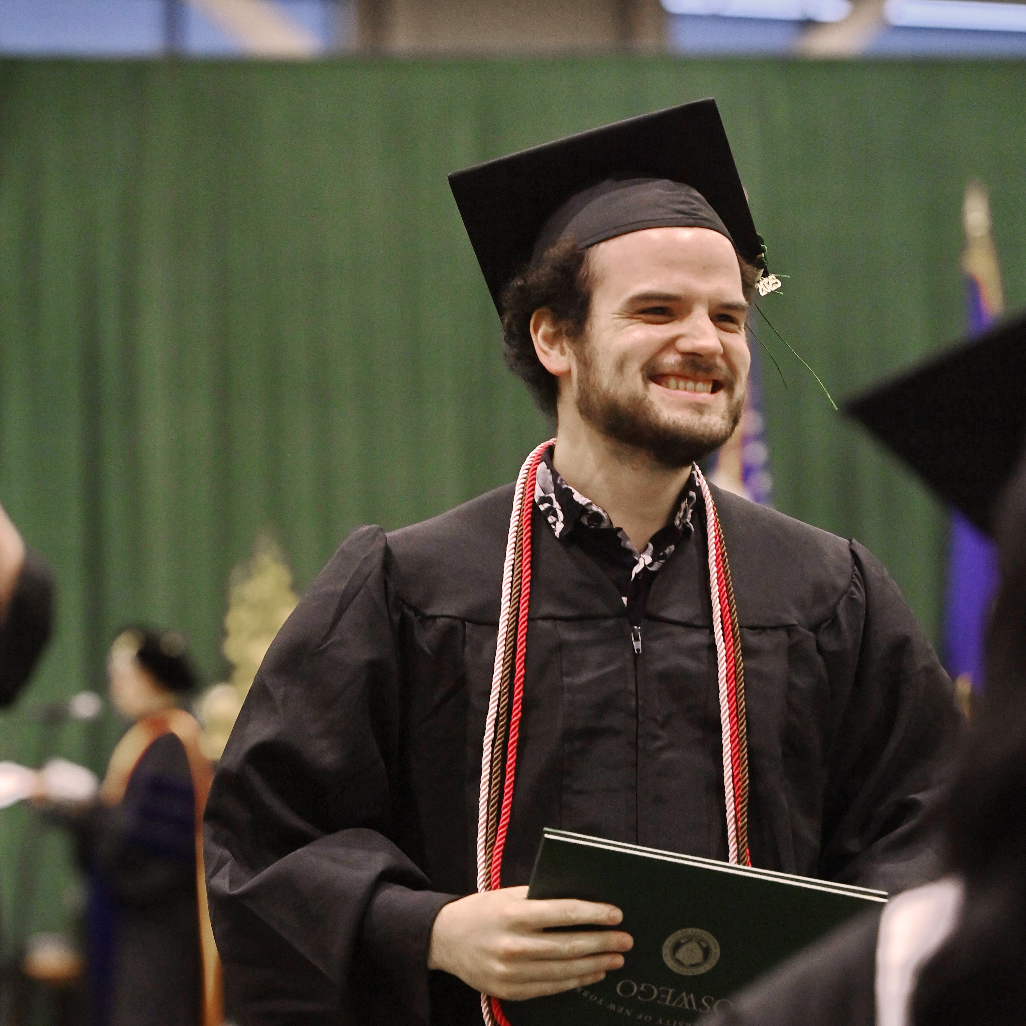 Joshua smiling in his cap and gown, holding his diploma at graduation.